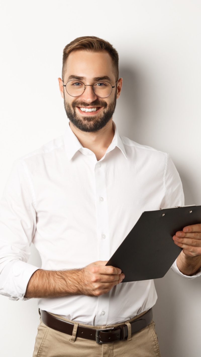 Handsome manager in glasses working, using clipboard, standing over white background.